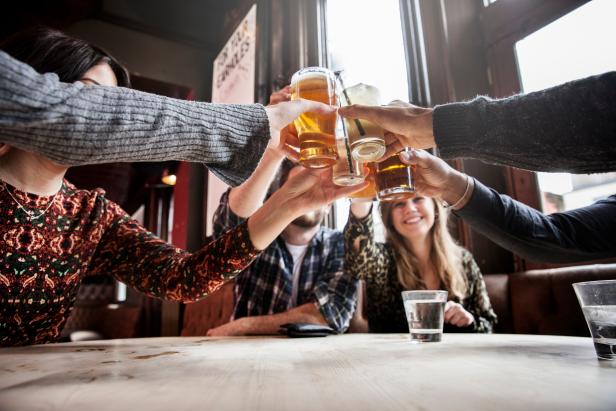 Group of friends toasting in a pub, holding their glasses high above the table